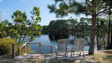 Terraza junto al lago con barandilla de madera y dos sillas Adirondack mirando al agua.
