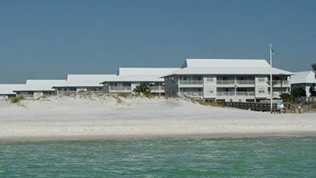 Et hotel ved stranden med flere bygninger med hvide tage, en sandstrand og klart, blåt vand.