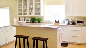 A kitchen with white cabinets, a central island with stools, a sink, and a microwave.