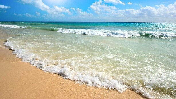 A beach with clear turquoise water and a sandy shore under a bright sun.