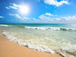 A beach with clear water, waves, and a sunny sky.
