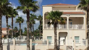 A two-story building with a balcony, surrounded by palm trees, and a gated pool area.