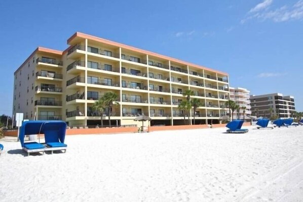 Un hotel de varios pisos con balcones, situado en una playa con tumbonas y sombrillas.