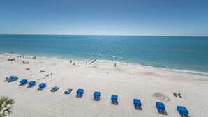 Una playa con hileras de sillas y sombrillas azules, una orilla arenosa y el océano al fondo.