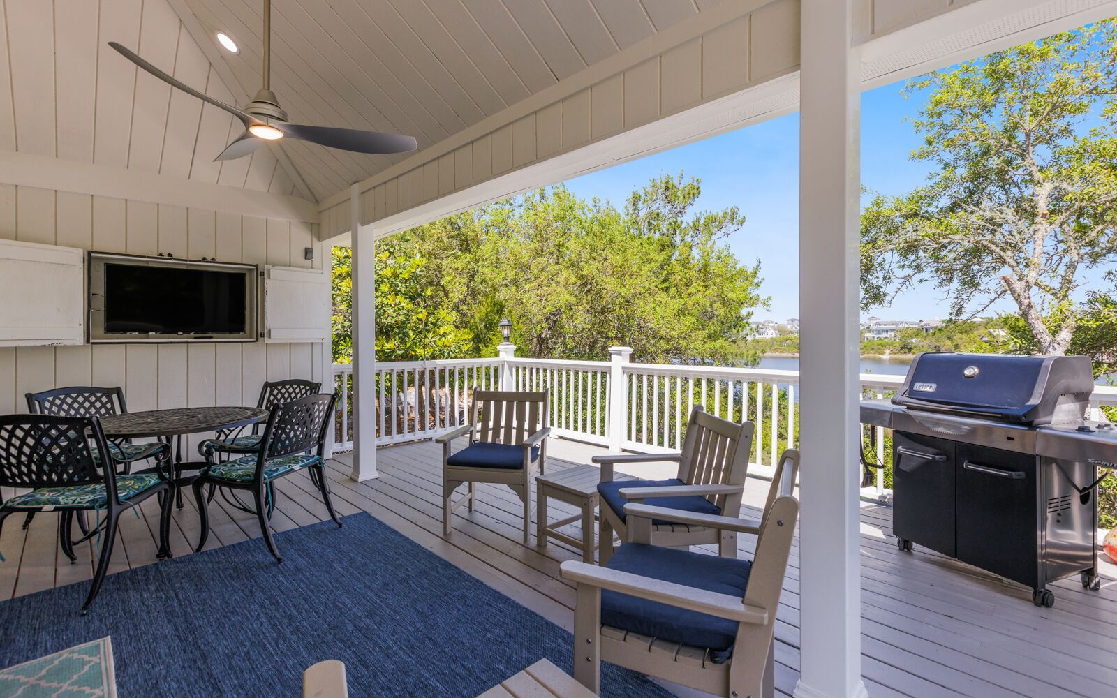 A covered outdoor patio with a table and chairs, a grill, and a TV mounted on the wall.