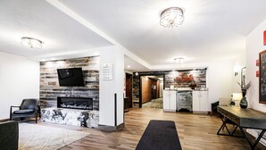 A modern living room with a fireplace, a flat-screen TV mounted on a wooden wall, a dining area with a wooden table and chairs, and a kitchen area with a stone backsplash. - Managed by Park City Lodging-Main St. Area Condo on Free Shuttle/ Walk to Lift (Park City)