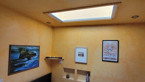 Een slaapkamer met een bed, dakraam, schilderij en poster aan de muur.