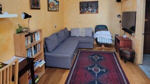 Een woonkamer met een bank, een boekenkast, een televisie en een kamerbreed tapijt met een patroon.