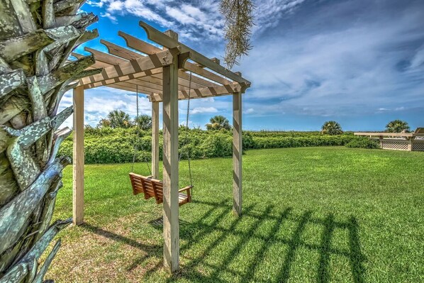 Une pergola en bois avec une balançoire, située dans une cour bien entretenue et recouverte de gazon.