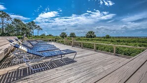 Un pontile in legno con poltrone da relax blu e vista su un prato curato e alberi.