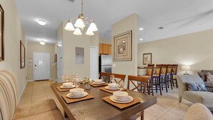 A dining area with a wooden table set for four, surrounded by chairs. There is a kitchen area with wooden cabinets and a refrigerator in the background. - Paradise Palms Resort 4 Bedroom Private Pool Townhome (Kissimmee)