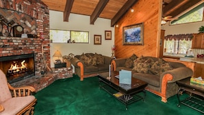 A cozy living room with a brick fireplace, green carpet, and wooden furniture. - Summit Adventure - Walk to Snow Summit, Game Room, Pool Table, BBQ (Big Bear Lake)