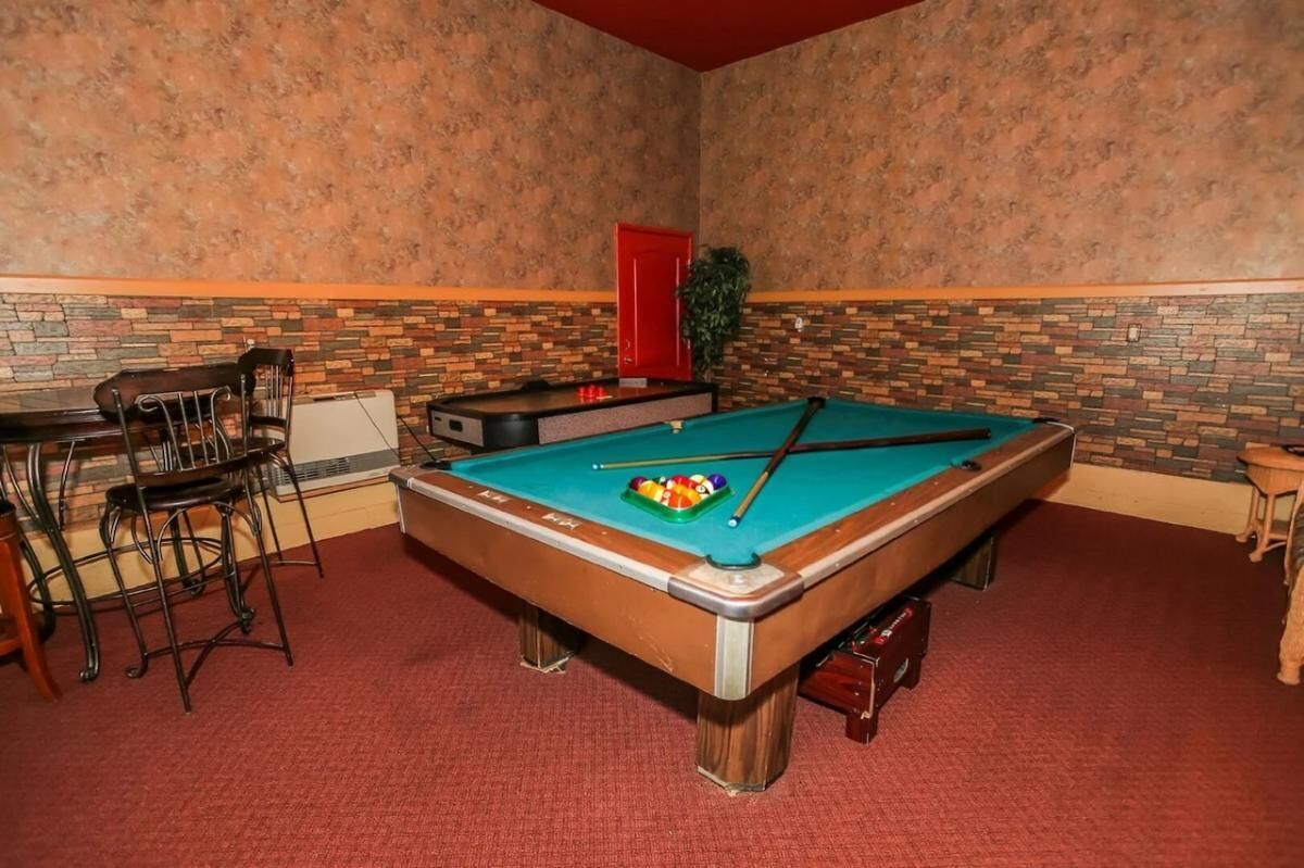Une table de billard avec une porte rouge et une petite table avec des chaises, dans une pièce aux murs décorés de motifs.