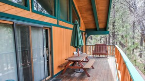 A wooden deck with a picnic table and chairs, a green umbrella, and a view of trees. - Summit Adventure - Walk to Snow Summit, Game Room, Pool Table, BBQ (Big Bear Lake)