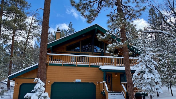 A two-story log cabin with a green roof and a balcony, surrounded by snow-covered trees. - Summit Adventure - Walk to Snow Summit, Game Room, Pool Table, BBQ (Big Bear Lake)