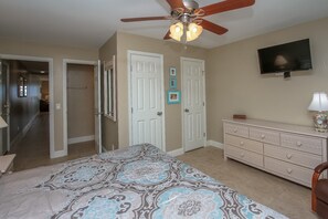 A bedroom with a bed, a dresser, a ceiling fan, and a hallway leading to another room.
