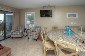 A dining area with a table and chairs, a television on the wall, and a window with blinds.