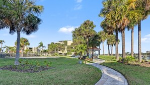 Un sendero serpentea por una zona verdejante con palmeras y un edificio al fondo.