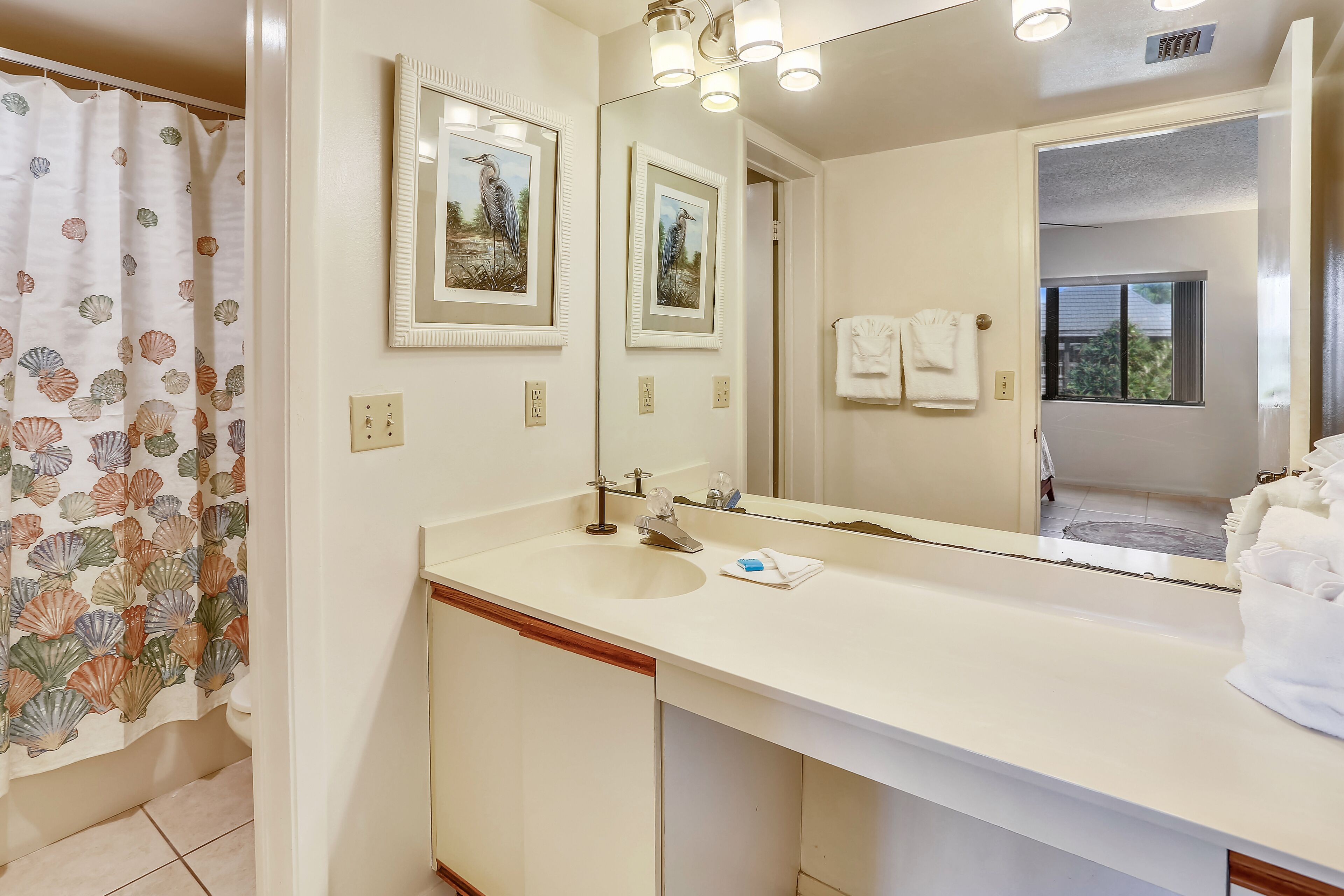 Une salle de bain avec un lavabo blanc, un miroir et un rideau de douche orné d’un motif de coquillages.