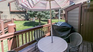 Una terraza con una mesa, sillas, una sombrilla y una parrilla.