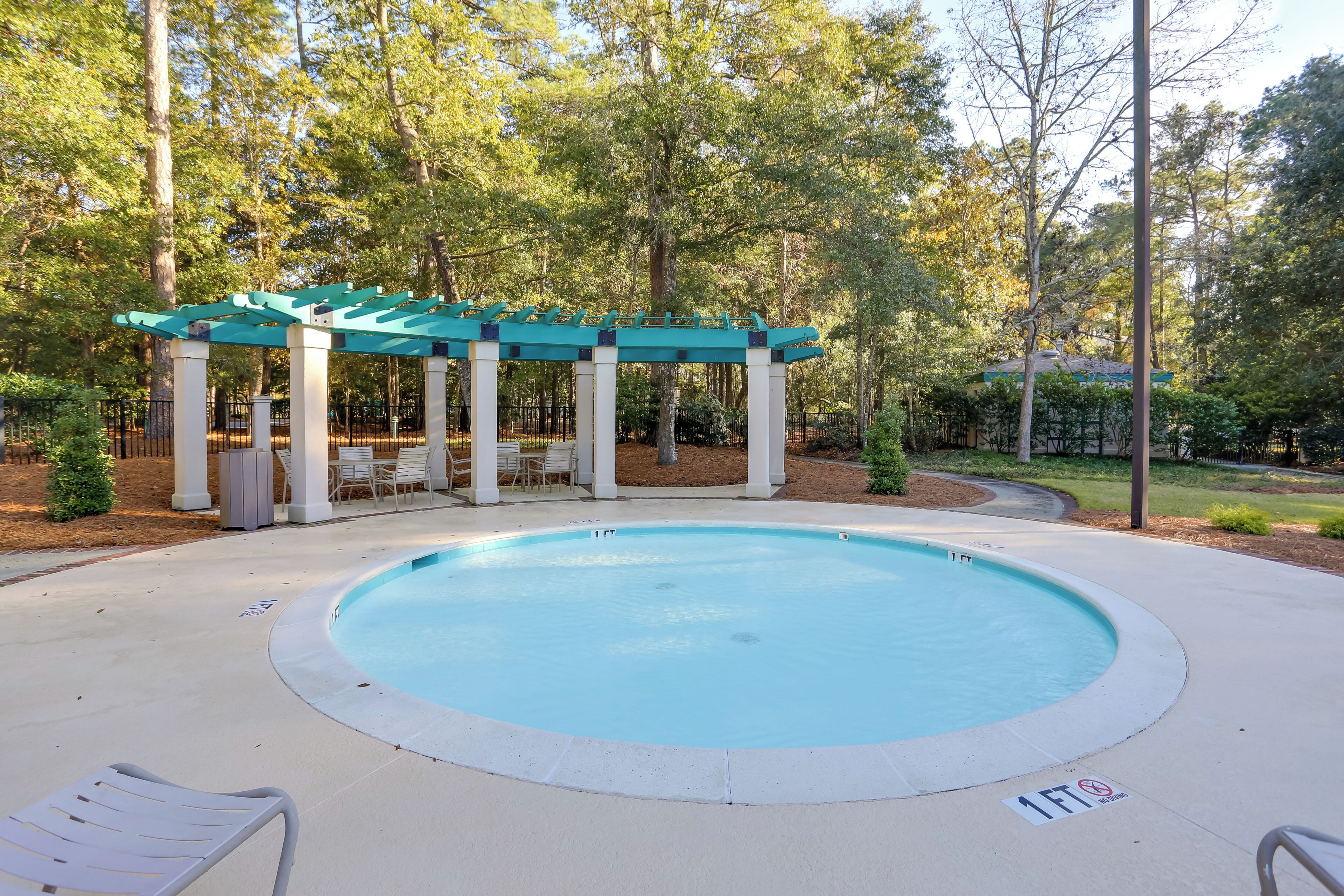 A circular pool with a surrounding deck, a covered seating area, and a 1-foot no-entry sign.