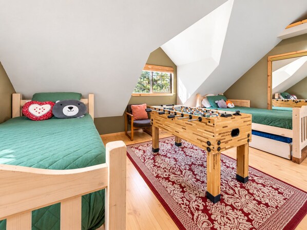 Dormitorio tipo loft con dos camas, una mesa de futbolín y un ventanal con vistas.