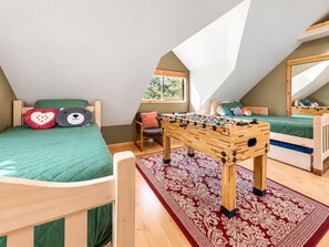 A loft bedroom with two beds, a foosball table, and a window with a view.