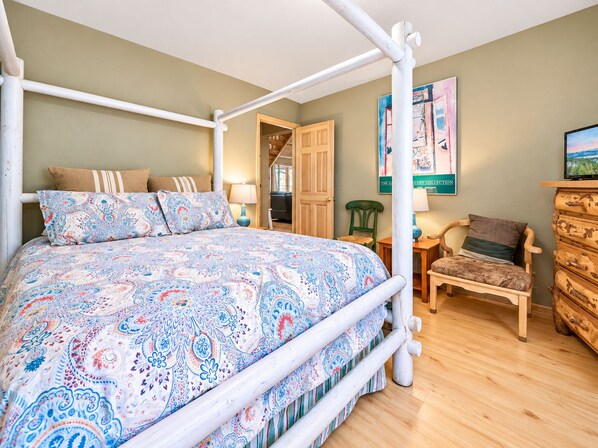 A bedroom with a four-poster bed, a wooden dresser, a chair, and a painting on the wall.