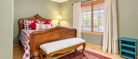 Une chambre à coucher avec un lit en bois, un banc, une fenêtre avec des rideaux et une lampe.