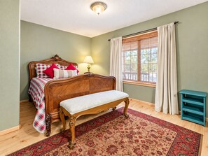 A bedroom with a wooden bed, a bench, a window with curtains, and a lamp.