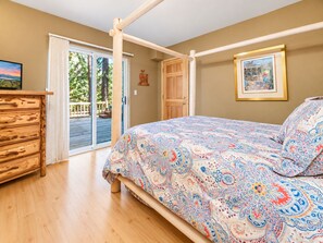 A bedroom with a bed, wooden dresser, and a door leading to an outdoor deck.
