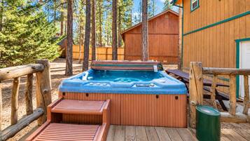 Una terraza de madera con un jacuzzi, bancos de madera y un bote de basura.