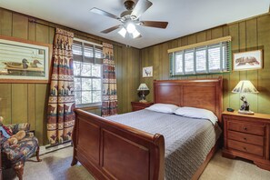 Un dormitorio con cama de madera, una mesita de noche con lámpara, una silla y una ventana con persianas.