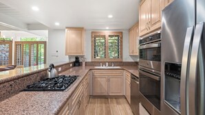 A modern kitchen with granite countertops, stainless steel appliances, wooden cabinets, and a window with a view of greenery.