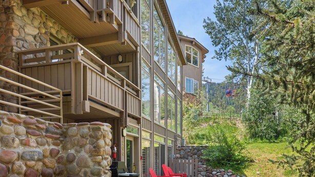 A stone exterior wall, a wooden deck with red chairs, and a clear view of the surrounding greenery.