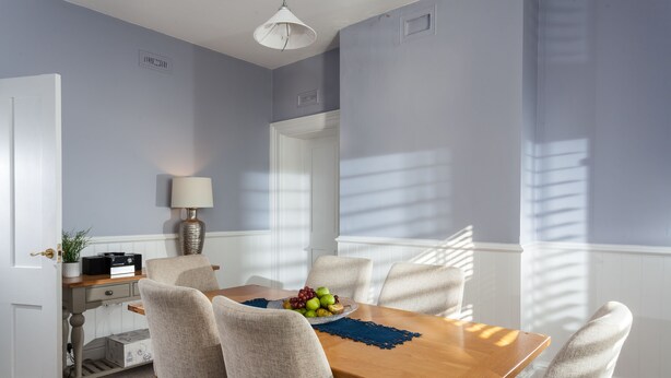 A dining area with a wooden table, six chairs, a fruit bowl, and a lamp.