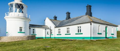 A lighthouse with a white tower and a white building with green trim.