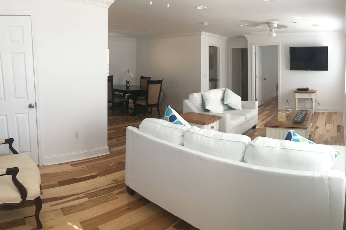 A living room with a white sofa, a wooden dining table with chairs, and a white armchair.