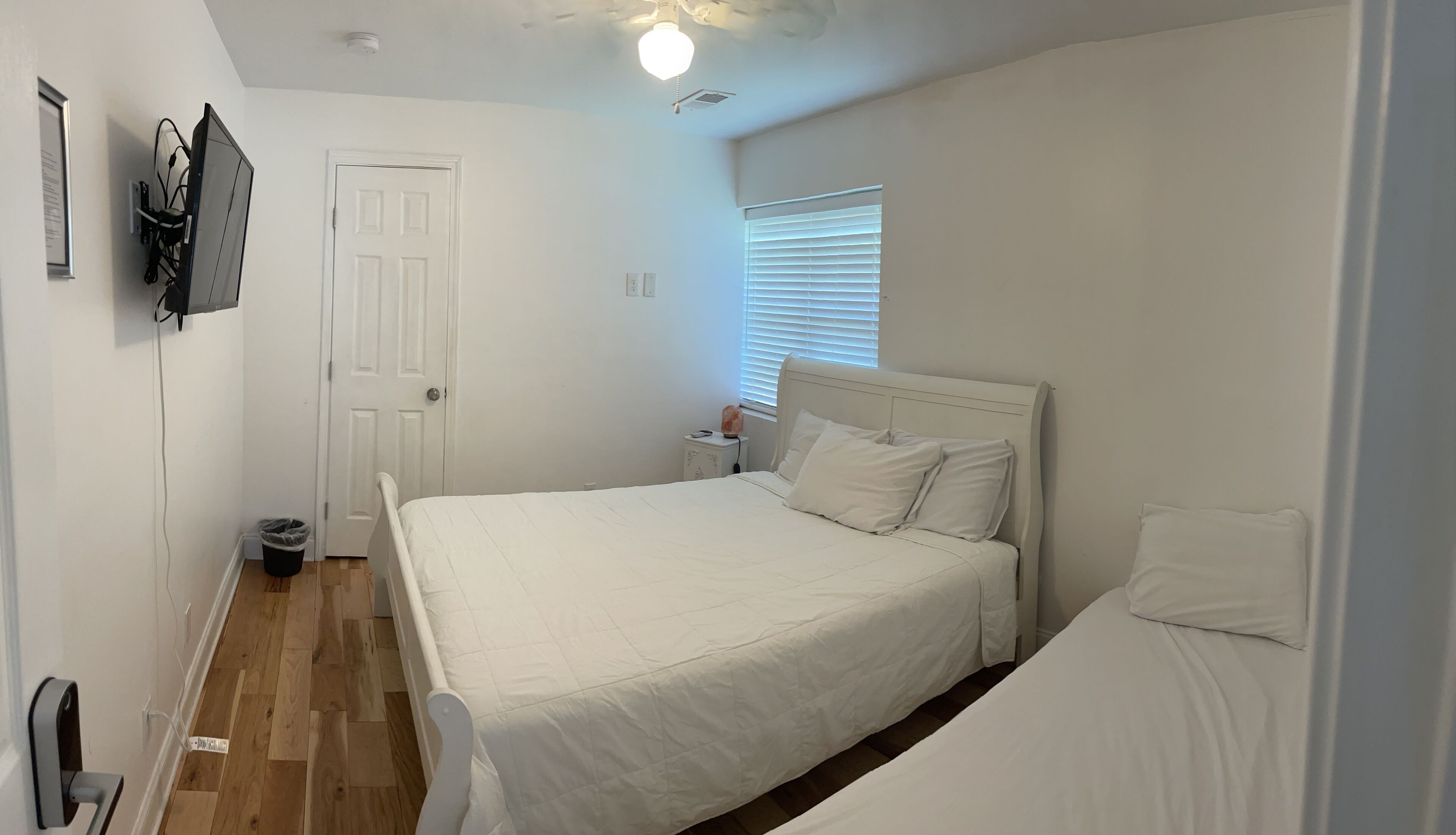 A bedroom with a bed, a nightstand, a heater, a door, and a window with blinds.