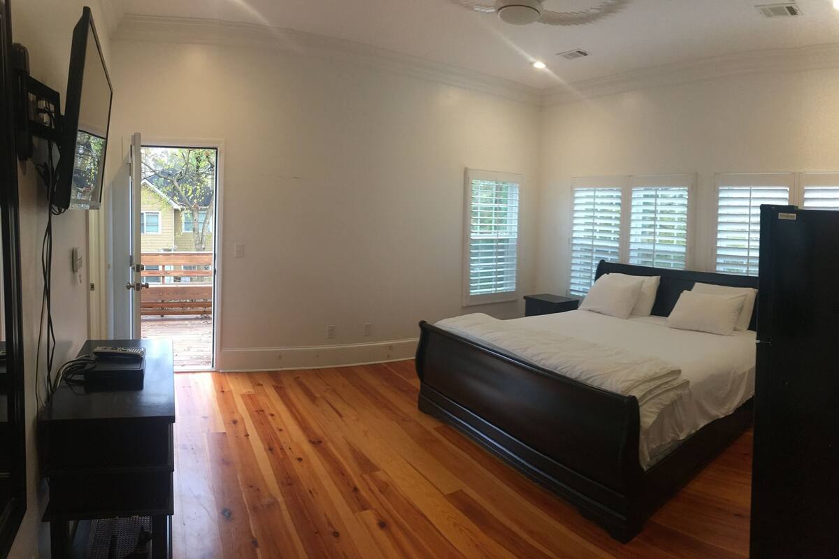 A bedroom with a wooden floor, a bed with white bedding, a nightstand, and a black dresser.