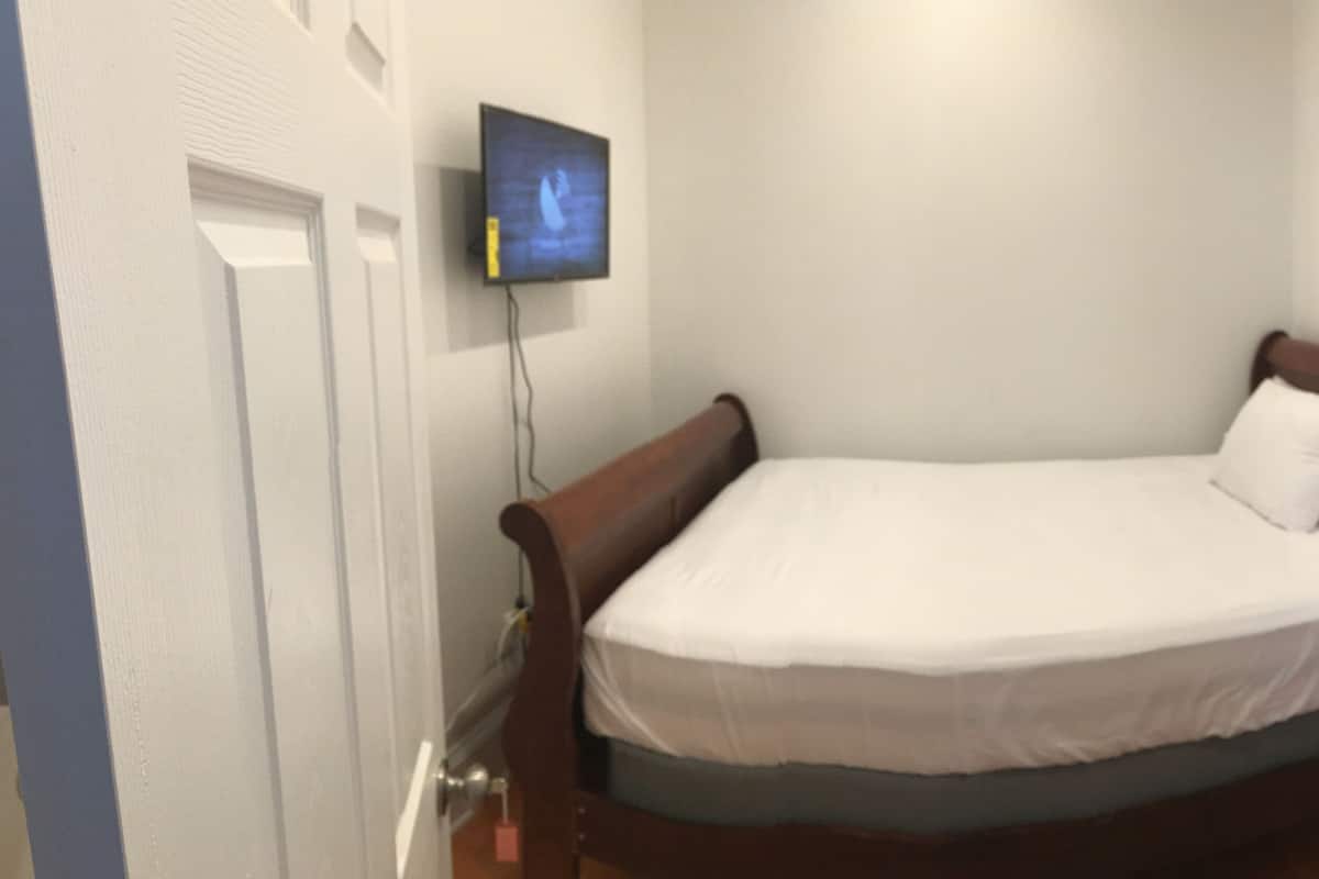A bedroom with a wooden bed, a wall-mounted TV, and a small bedside table with two bottles.