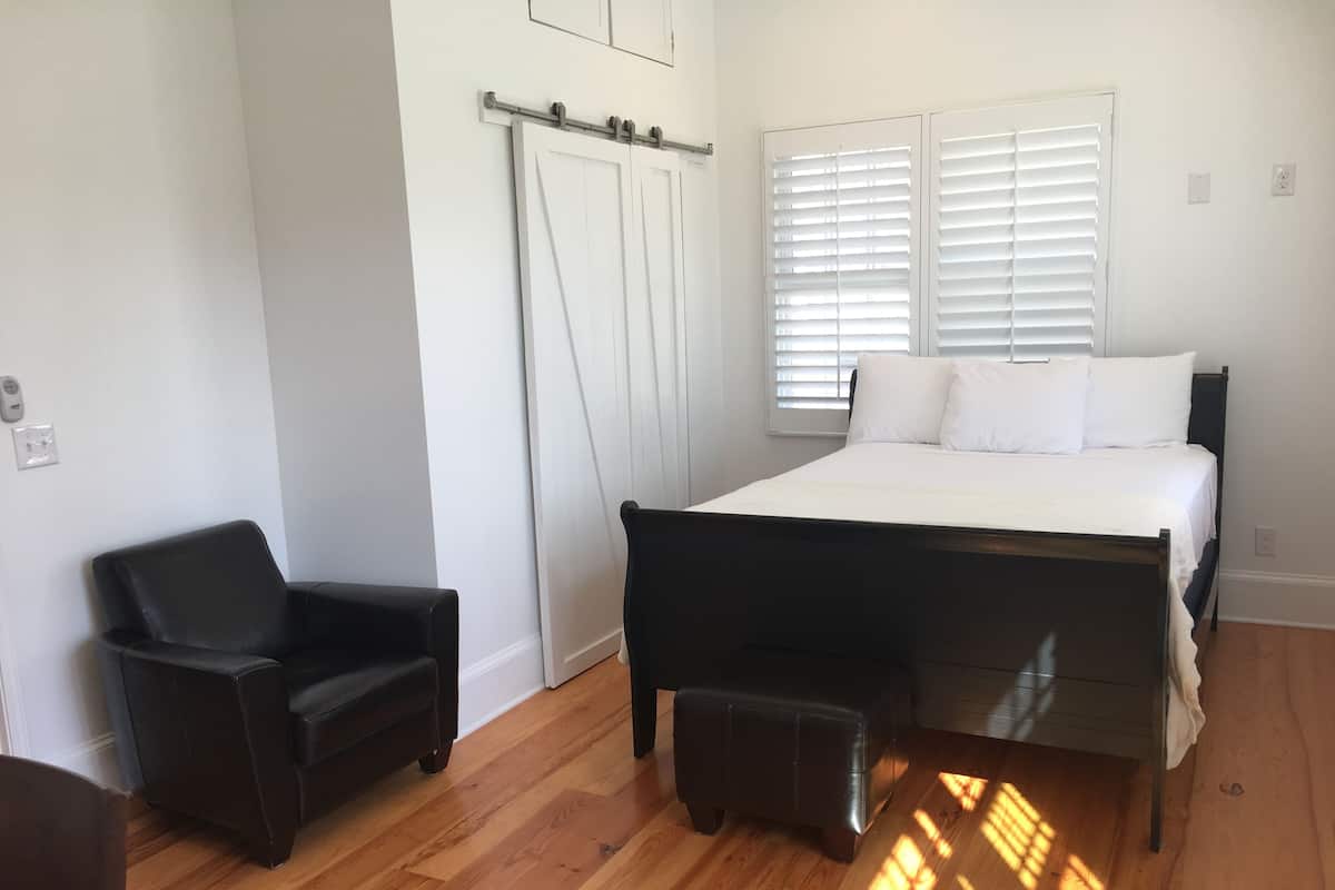 A bedroom with a bed, a chair, a bench, a wardrobe, and a window with blinds.