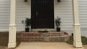 A white building with a black door, number 1000, and two potted plants on the front steps. - Alecia B&B (Atlanta)