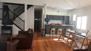 A spacious living room with a brown leather sofa, wooden flooring, a staircase, a kitchen with bar stools, and a dining area with a table and chairs. - Alecia B&B (Atlanta)