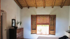 A bedroom with a wooden ceiling, a bed, a dresser, a window with shutters, and a door. - The cortijo, a spacious, beautifully designed holiday home & pool in Extremadura (Caceres)