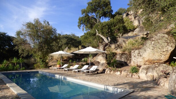 A swimming pool with lounge chairs and umbrellas, surrounded by a rocky landscape and trees. - The cortijo, a spacious, beautifully designed holiday home & pool in Extremadura (Caceres)