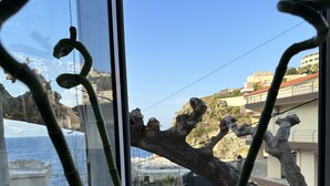 Ein Fenster mit Blick auf einen Baumast, ein Blumentopf auf der Fensterbank und ein klarer, blauer Himmel.