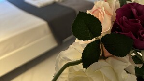Ein Hotelzimmer mit einem Bett, einem Nachttisch mit Blumenvase und einem Fenster mit Vorhängen.