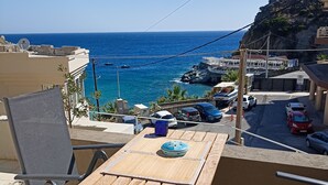 Ein Holztisch mit Stühlen auf einem Balkon mit Blick auf eine Küstenlandschaft, einschließlich Gebäude und geparkte Autos.