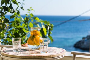 Uma mesa com uma jarra de suco de laranja, dois copos e vista para o oceano.